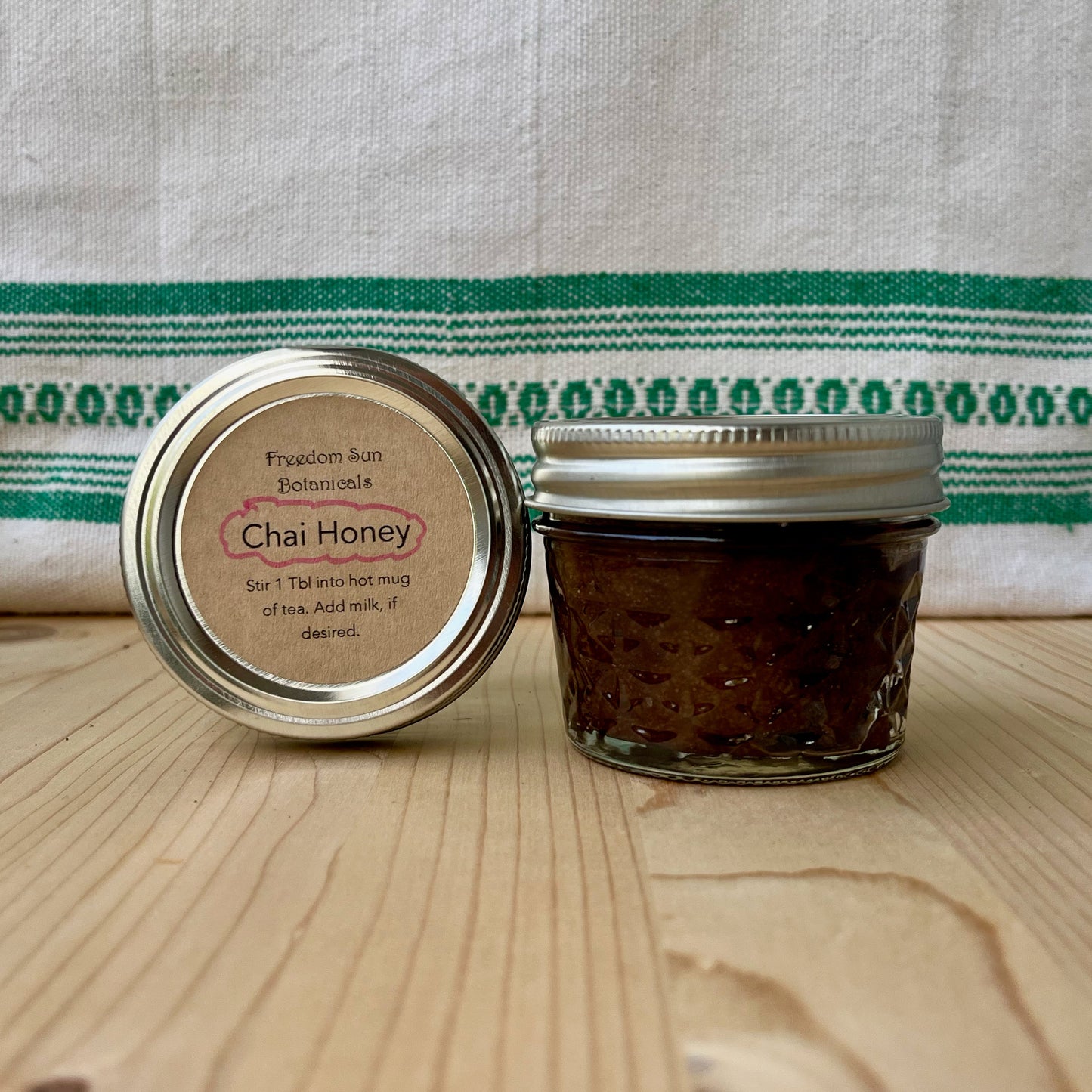Jar of Chai Honey on a wooden surface with a green and white striped towel in the background