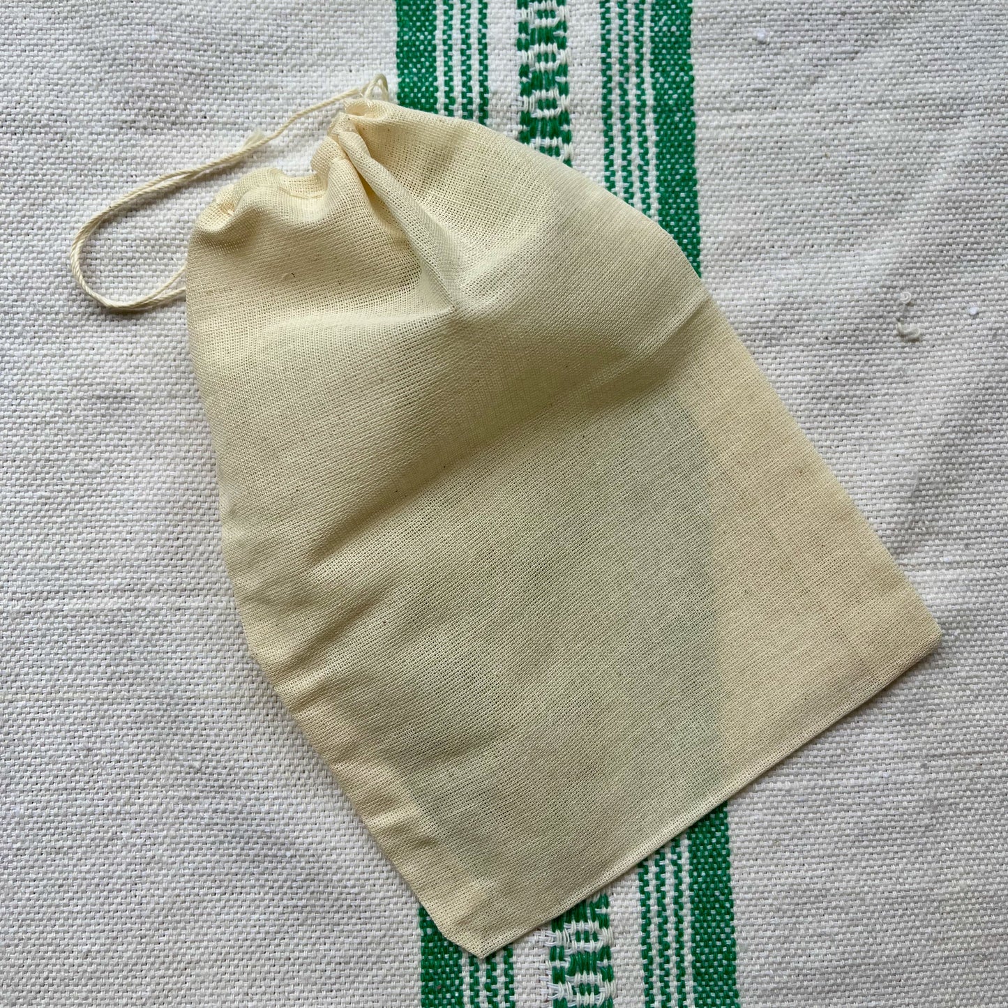 Beige drawstring bag on a textured fabric background with green stripes