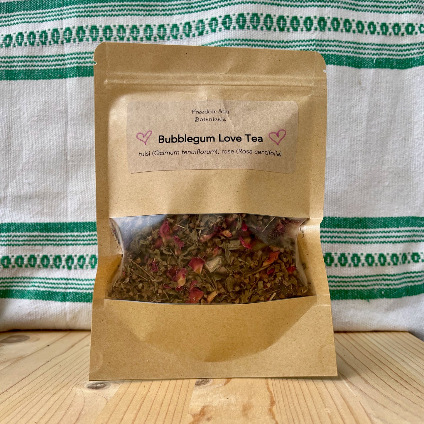 Bag of Bubblegum Love Tea on a wooden surface with a striped cloth background