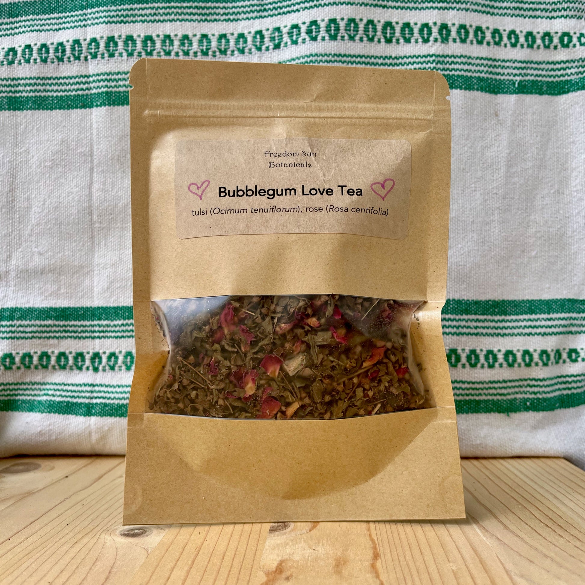 Bag of Bubblegum Love Tea on a wooden surface with a striped cloth background