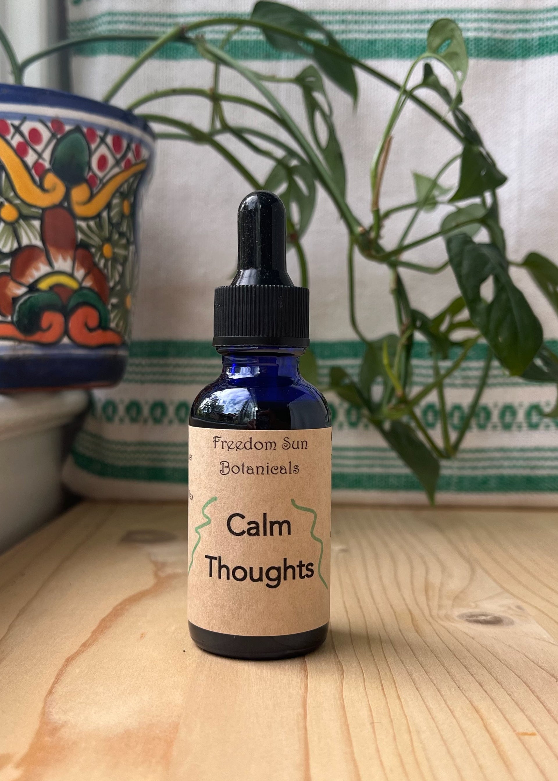 Bottle of Calm Thoughts tincture on a wooden surface with a plant and decorative pot in the background.