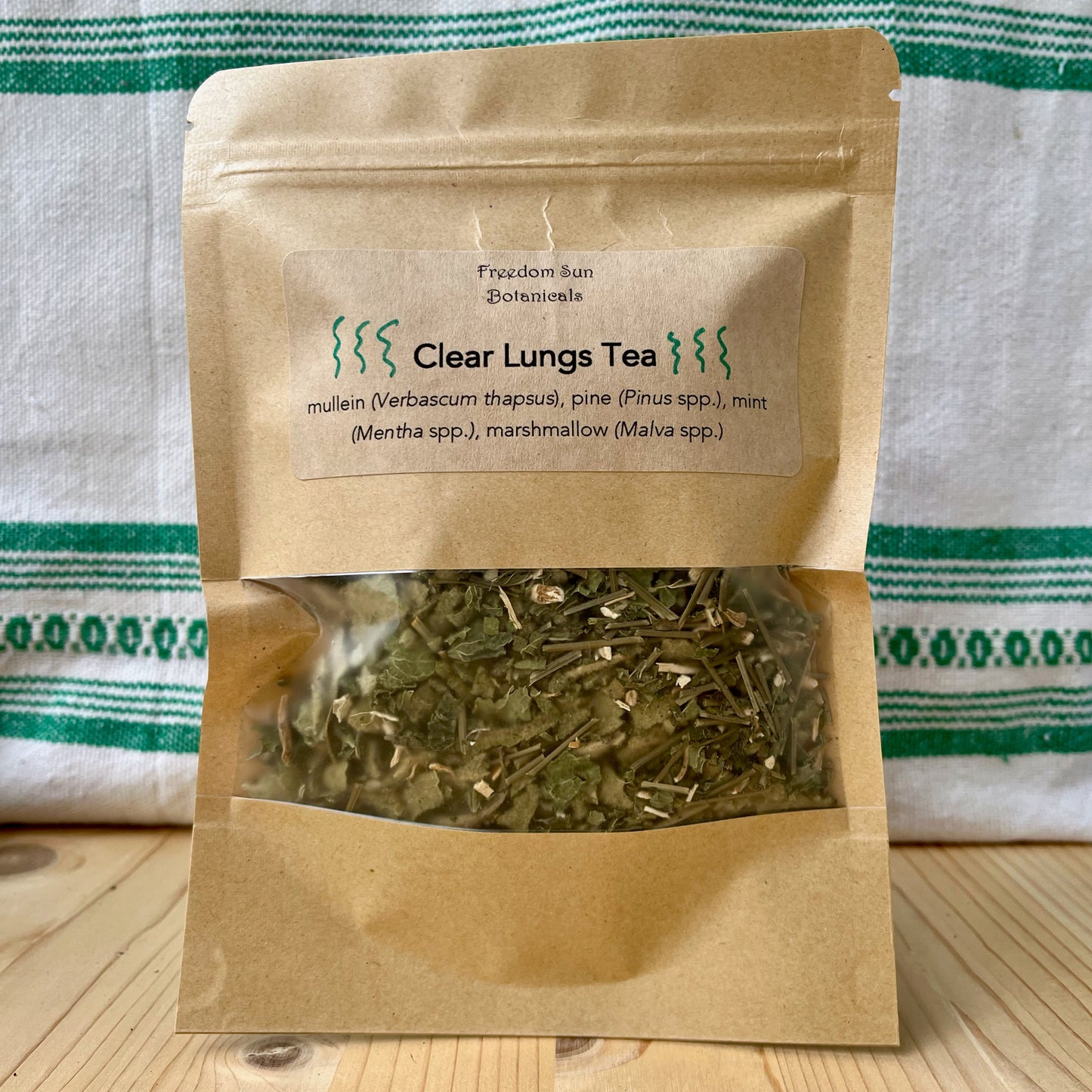 Clear Lungs Tea package with tea leaves on a wooden surface and striped fabric background