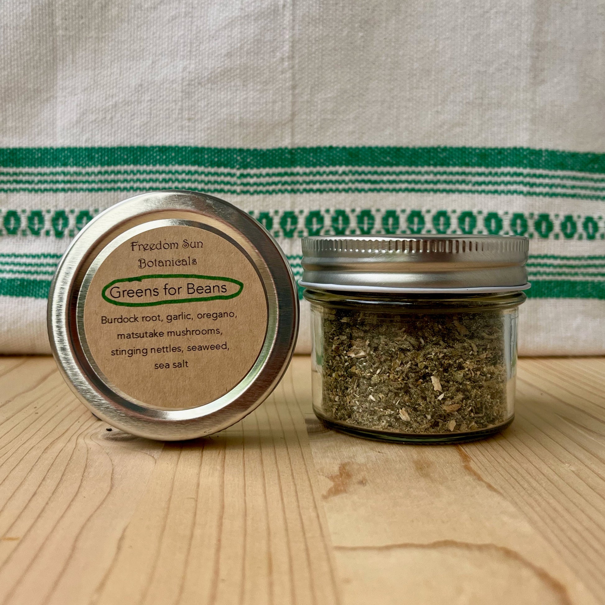 Two small jars with metal lids on a wooden surface with a green and white striped cloth in the background.