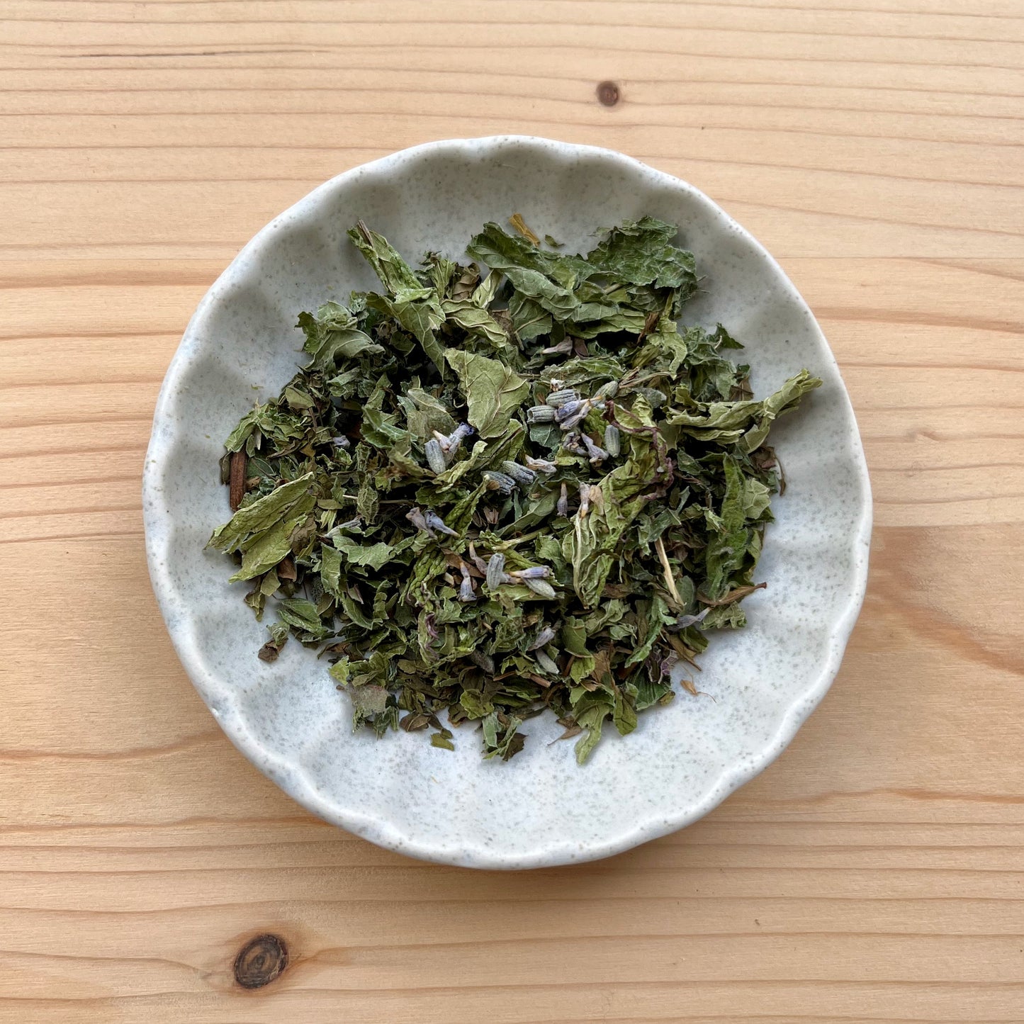 Dried green leaves in a small white bowl on a wooden surface