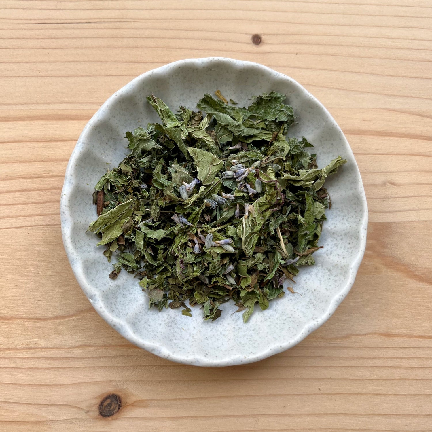 Dried green leaves in a small white bowl on a wooden surface