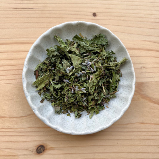 Dried green leaves in a small white bowl on a wooden surface