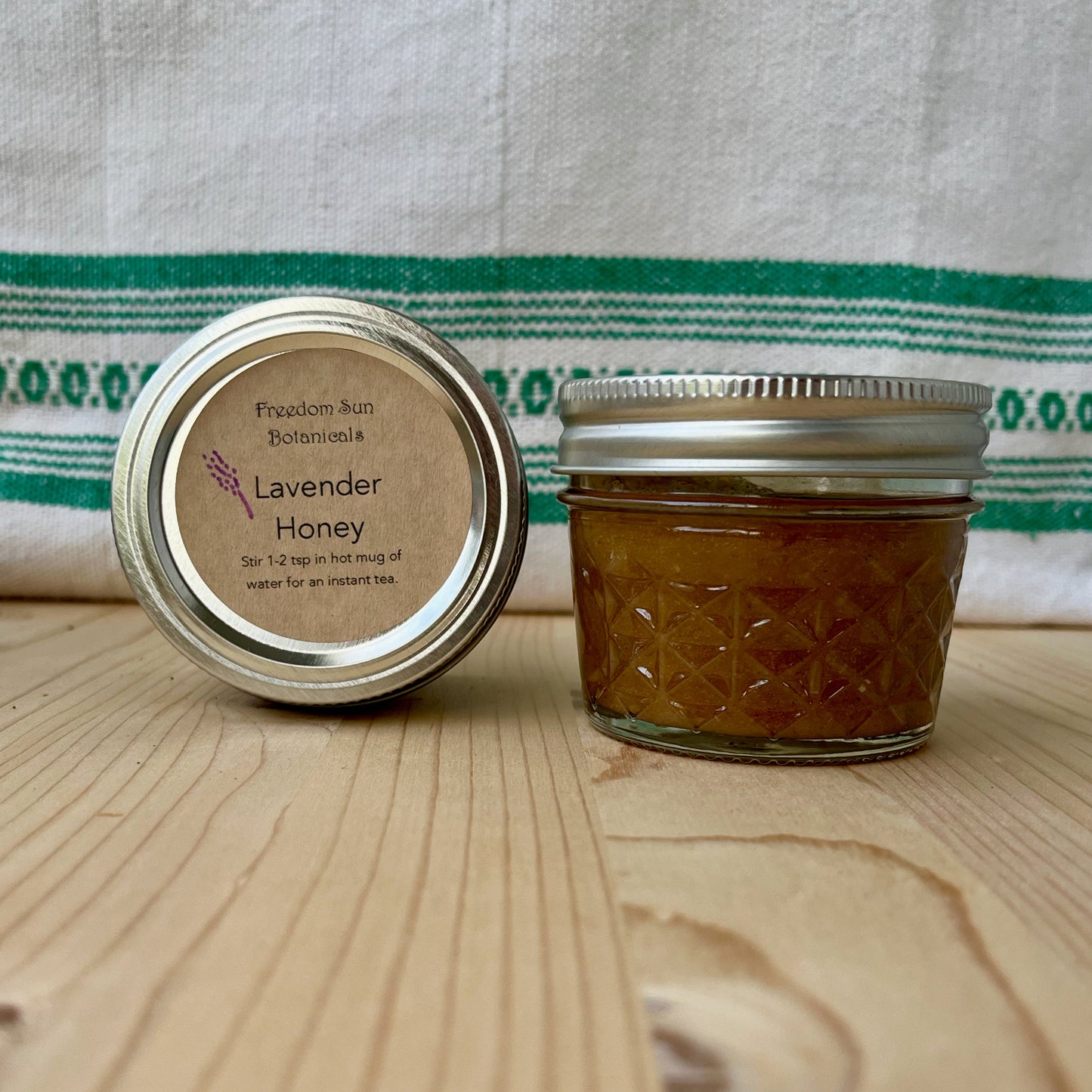 Jar of lavender honey with a lid on a wooden surface and fabric background