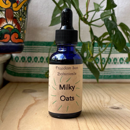 Bottle of 'Milky Oats' with a dropper on a wooden surface with a plant and decorative item in the background.