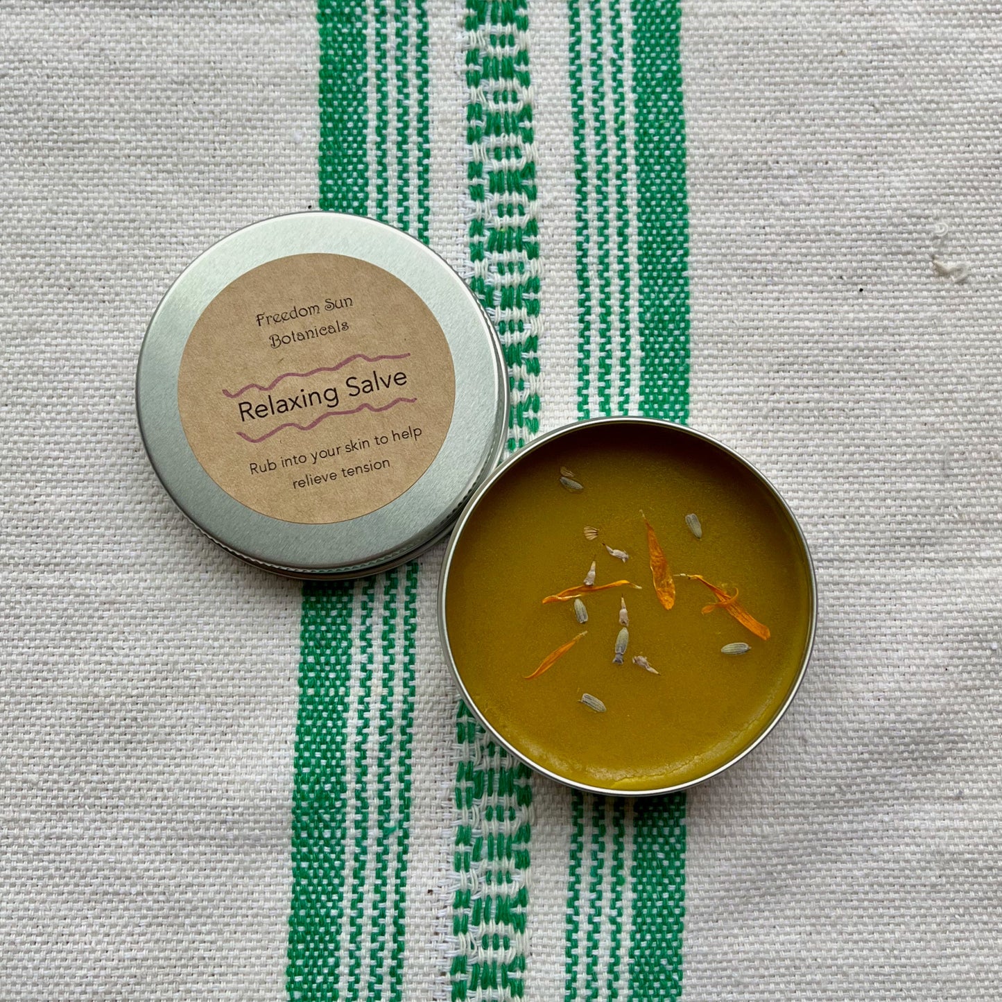 Tin of salve with a lid on a textured fabric background