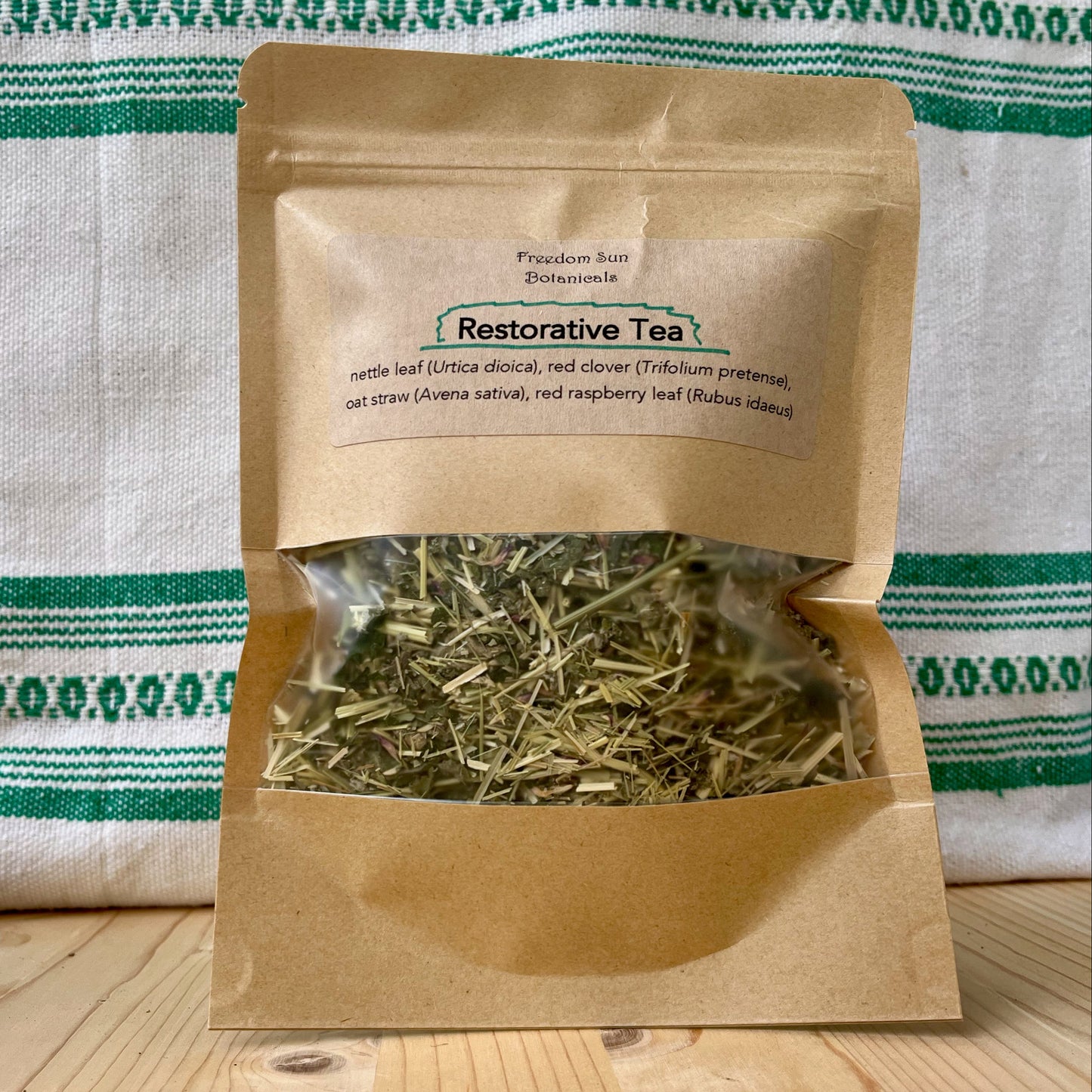 Brown paper bag with 'Restorative Tea' label on a wooden surface with a striped fabric background