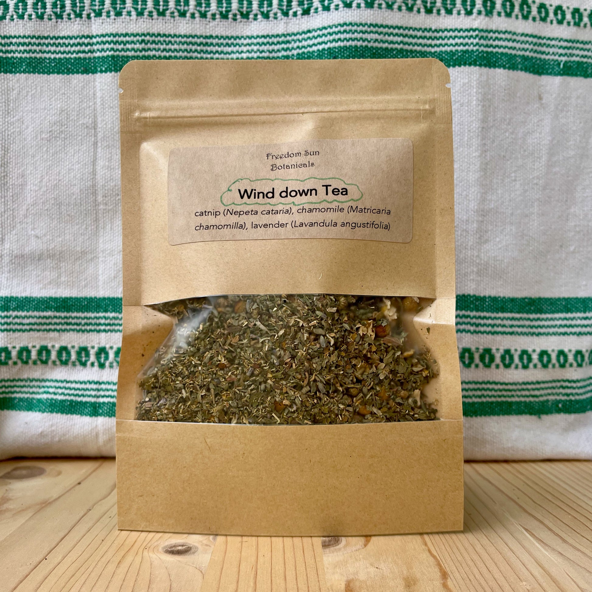Tea package labeled 'Wind down Tea' on a wooden surface with a green and white striped towel in the background.